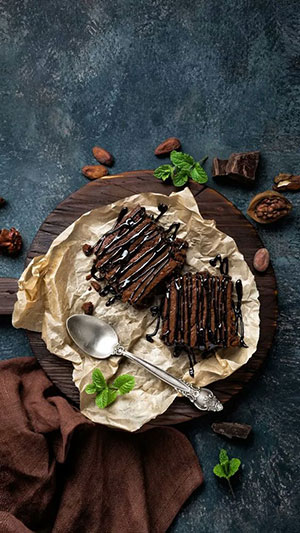 two chocolate brownies on a wooden plate with a spoon next to them